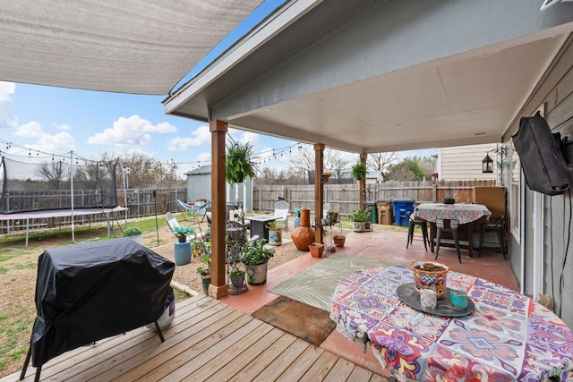 wooden terrace with a patio, a fenced backyard, grilling area, a trampoline, and outdoor dining space