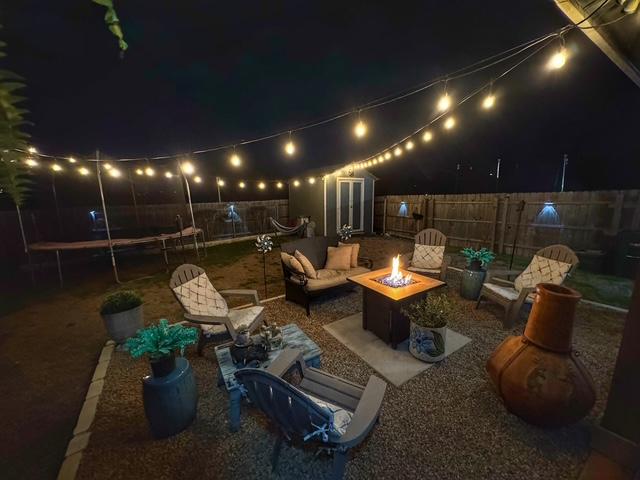 patio at twilight featuring a fenced backyard, an outdoor structure, a storage unit, a trampoline, and an outdoor living space with a fire pit