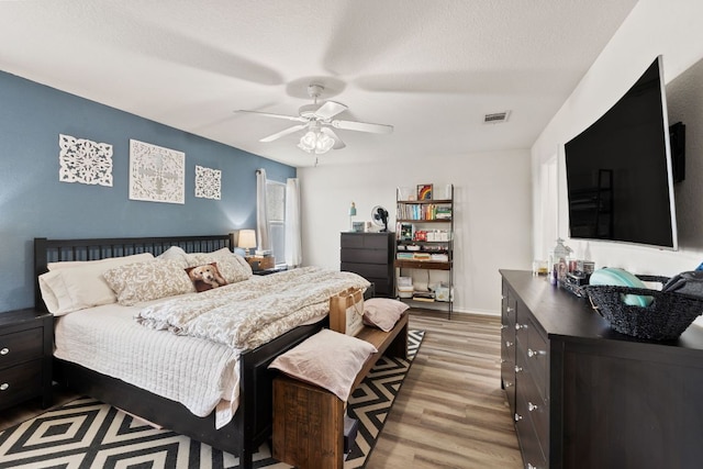 bedroom featuring ceiling fan, a textured ceiling, wood finished floors, visible vents, and baseboards