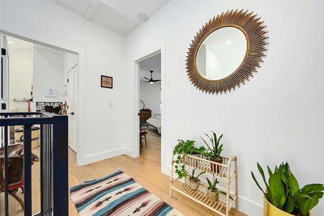 hallway with an upstairs landing, baseboards, and light wood-type flooring