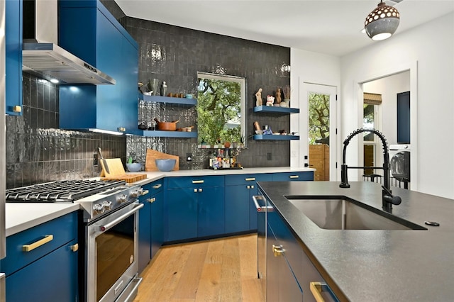 kitchen featuring stainless steel gas range oven, a sink, blue cabinets, wall chimney exhaust hood, and open shelves