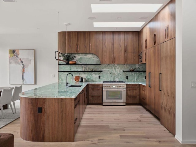 kitchen featuring a skylight, open shelves, backsplash, a sink, and high end stove