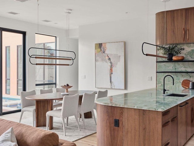 kitchen with light wood finished floors, visible vents, brown cabinets, light stone countertops, and a sink