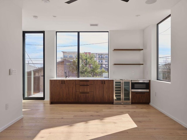 bar with light wood finished floors, ceiling fan, wine cooler, and stainless steel microwave