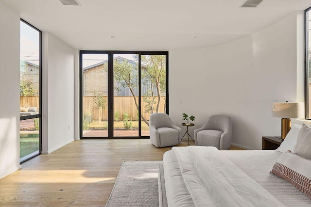 bedroom with access to outside, multiple windows, floor to ceiling windows, and wood finished floors