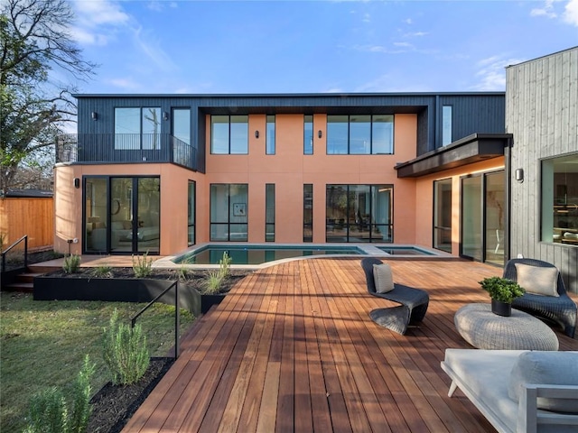 back of house with an in ground hot tub, a wooden deck, and an outdoor pool