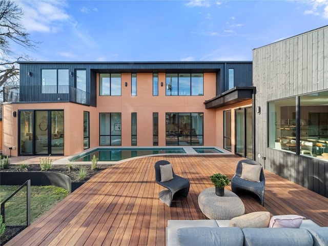 rear view of house with a balcony, an outdoor hot tub, and an outdoor pool