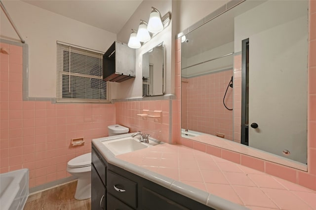 bathroom featuring toilet, a wainscoted wall, wood finished floors, tile walls, and a shower