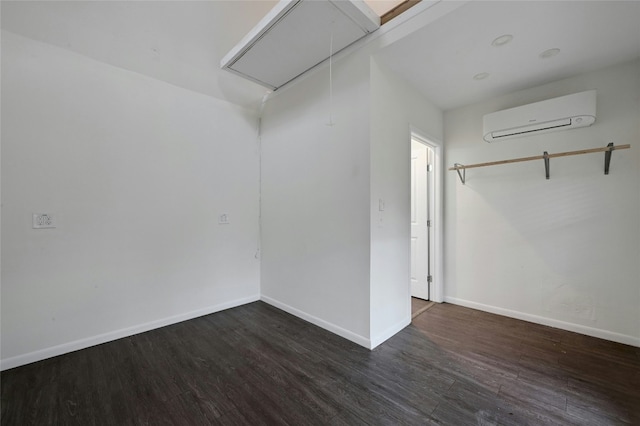 spare room featuring attic access, baseboards, wood finished floors, and a wall mounted AC