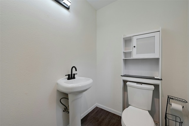 half bath featuring toilet, a sink, baseboards, and wood finished floors