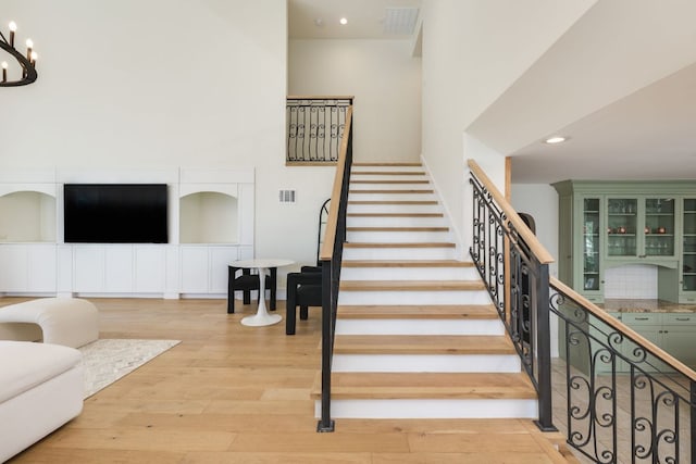 stairs featuring visible vents, wood finished floors, an inviting chandelier, a high ceiling, and recessed lighting