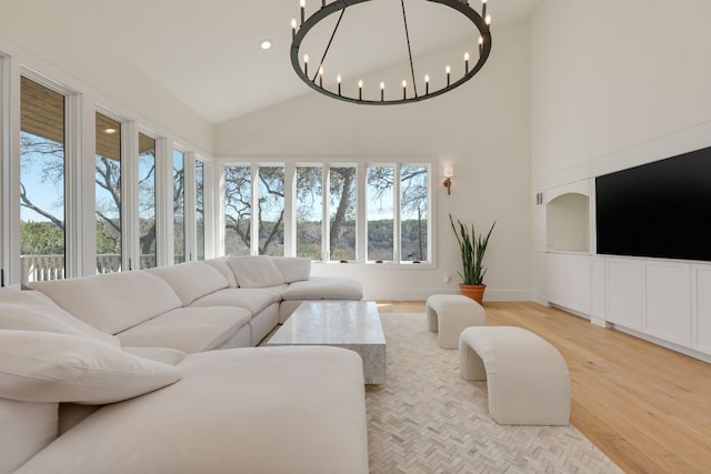 living area with a chandelier, high vaulted ceiling, light wood-style flooring, and baseboards