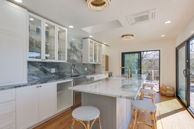 kitchen with light wood-style floors, white cabinetry, a sink, light stone countertops, and a kitchen breakfast bar