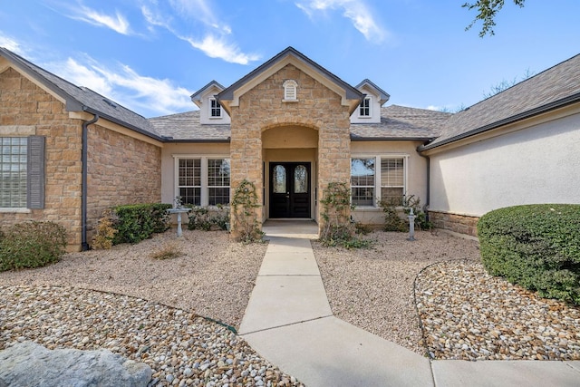 view of exterior entry featuring stone siding, french doors, a shingled roof, and stucco siding