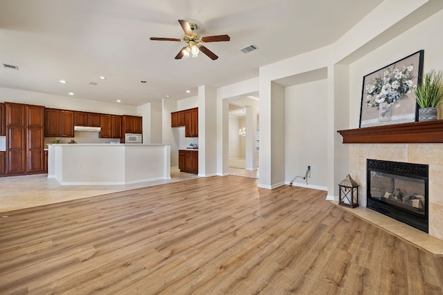 unfurnished living room with a tile fireplace, a ceiling fan, visible vents, baseboards, and light wood-type flooring