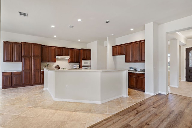 kitchen featuring recessed lighting, light countertops, visible vents, white microwave, and under cabinet range hood