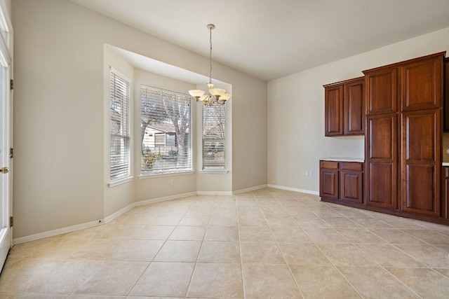 unfurnished dining area featuring a chandelier, light tile patterned floors, and baseboards