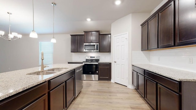 kitchen with light wood finished floors, light stone counters, appliances with stainless steel finishes, dark brown cabinets, and a sink