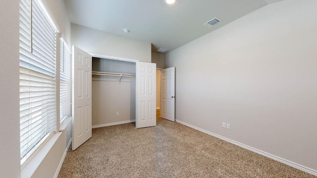 unfurnished bedroom featuring baseboards, visible vents, lofted ceiling, carpet floors, and a closet