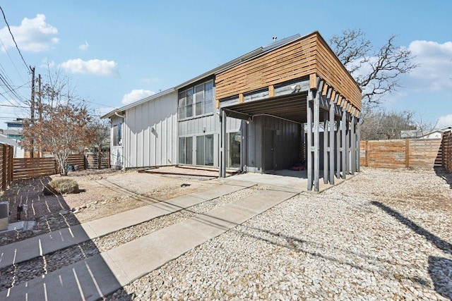 back of property with a carport, board and batten siding, and fence