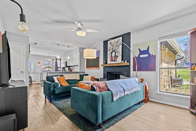 living area with light wood finished floors, visible vents, a ceiling fan, a large fireplace, and baseboards