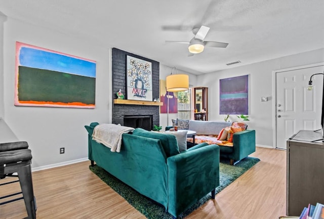 living room featuring a brick fireplace, visible vents, a ceiling fan, and wood finished floors