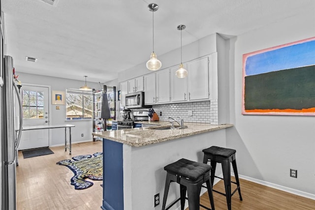 kitchen featuring backsplash, appliances with stainless steel finishes, white cabinetry, a sink, and light wood-type flooring