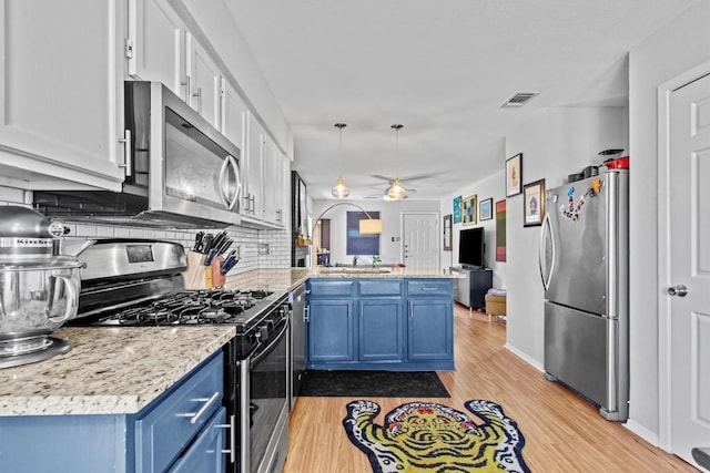 kitchen with decorative backsplash, light wood-style flooring, blue cabinets, a peninsula, and stainless steel appliances