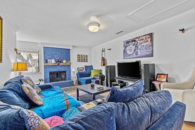 living area featuring attic access, a brick fireplace, visible vents, and wood finished floors