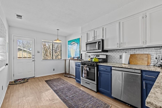 kitchen featuring blue cabinetry, stainless steel appliances, visible vents, backsplash, and light wood-type flooring