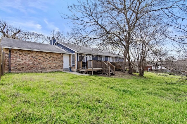 back of property with a deck, brick siding, a chimney, and a lawn