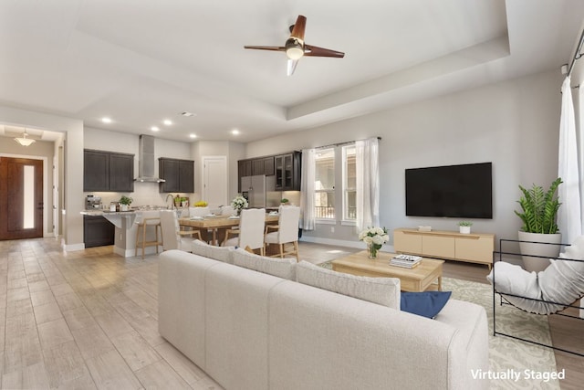 living area with recessed lighting, a raised ceiling, light wood-style flooring, and baseboards