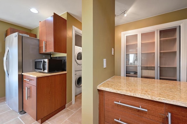 kitchen featuring stainless steel appliances, stacked washer / dryer, light tile patterned flooring, and brown cabinets