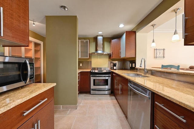 kitchen with wall chimney exhaust hood, appliances with stainless steel finishes, light stone counters, decorative light fixtures, and a sink