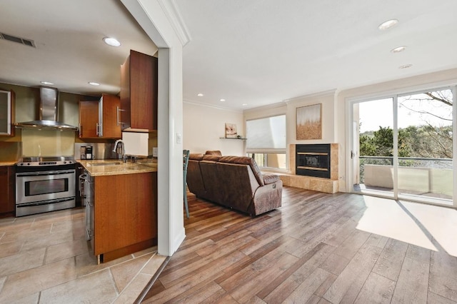 kitchen featuring visible vents, ornamental molding, stainless steel range with electric cooktop, a sink, and wall chimney exhaust hood