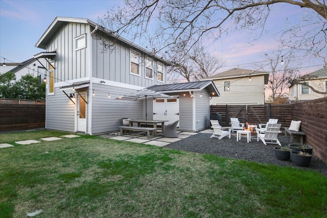 rear view of house with an outdoor fire pit, a fenced backyard, a lawn, board and batten siding, and a patio area