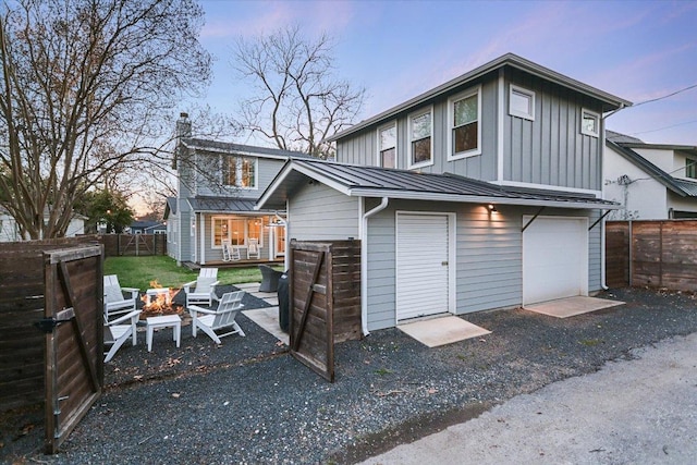 back of house at dusk with an outdoor fire pit, aphalt driveway, a standing seam roof, fence, and board and batten siding