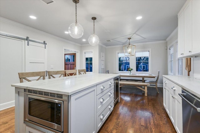 kitchen with a barn door, appliances with stainless steel finishes, white cabinets, and dark wood finished floors