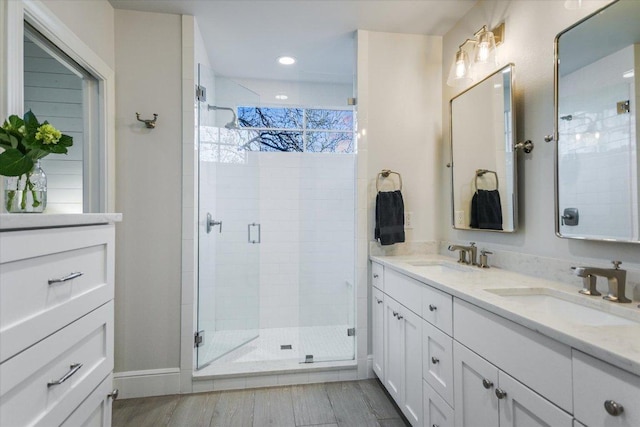 bathroom with double vanity, wood finished floors, a stall shower, and a sink