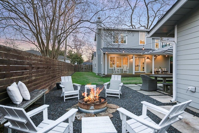 patio terrace at dusk featuring an outdoor fire pit, outdoor dining area, a fenced backyard, and a yard