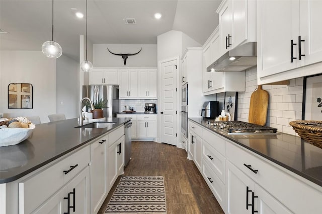 kitchen with stainless steel appliances, dark countertops, visible vents, a sink, and under cabinet range hood