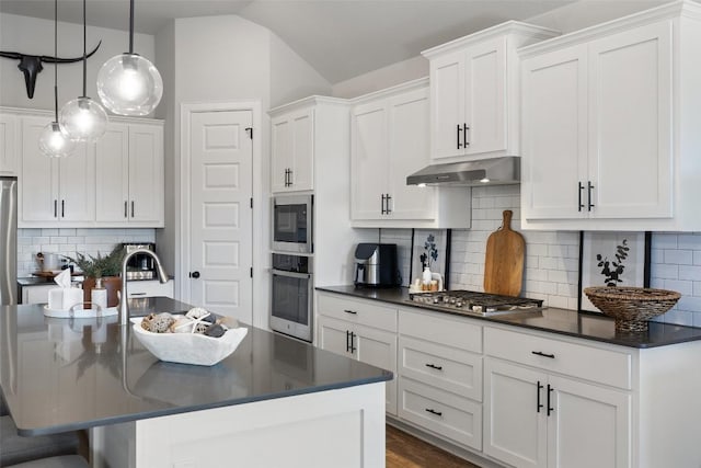 kitchen with stainless steel appliances, dark countertops, lofted ceiling, white cabinetry, and under cabinet range hood