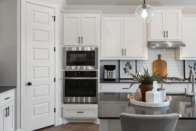 kitchen featuring built in microwave, dark countertops, stainless steel oven, and under cabinet range hood