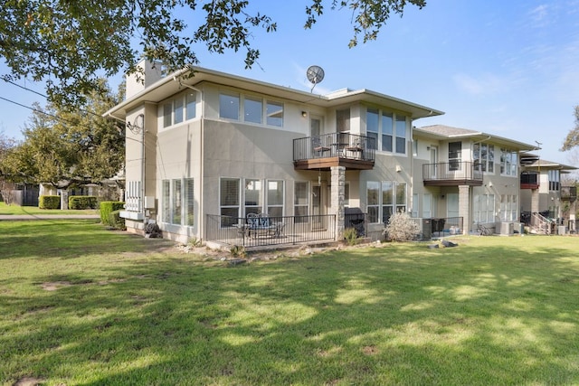 rear view of house featuring a chimney, a balcony, a lawn, and stucco siding