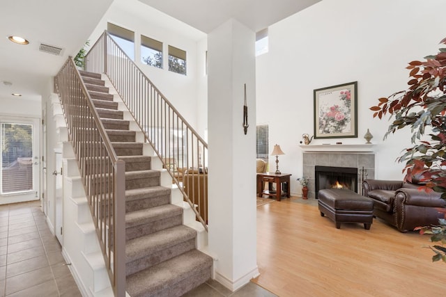 staircase with a fireplace, visible vents, a high ceiling, wood finished floors, and baseboards