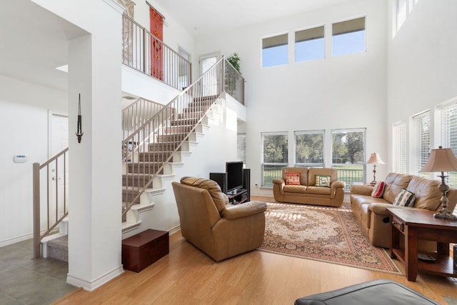 living area with stairs, a high ceiling, wood finished floors, and baseboards