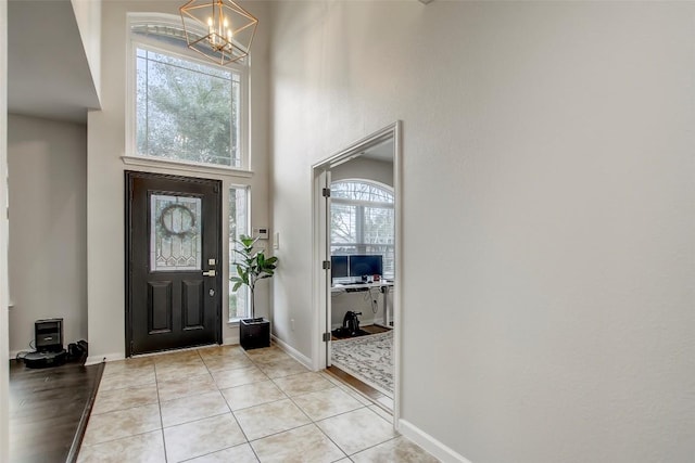 entrance foyer featuring a towering ceiling, light tile patterned floors, baseboards, and a notable chandelier