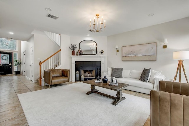 living area featuring tile patterned flooring, a notable chandelier, a fireplace, visible vents, and stairs