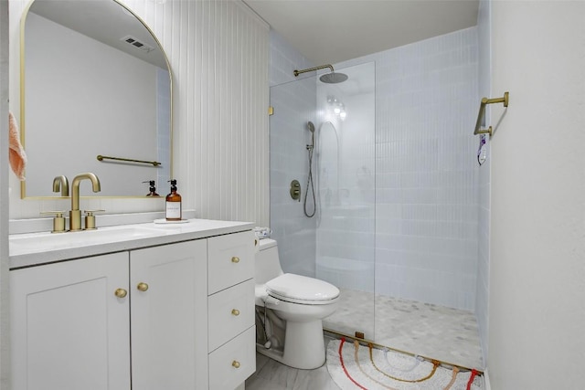 bathroom with visible vents, a tile shower, vanity, and toilet