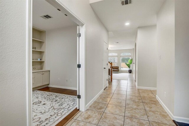 hall featuring visible vents, baseboards, and light tile patterned flooring